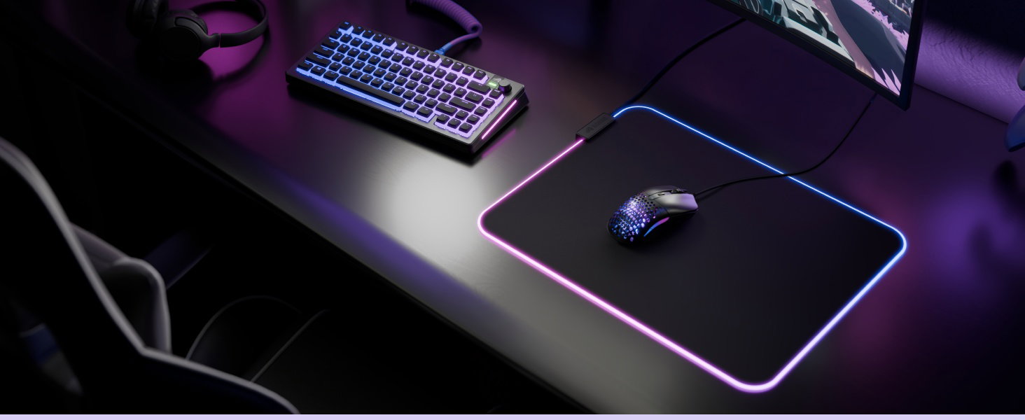 Configuration de bureau avec éclairage violet comprenant un clavier sans fil, une souris sans fil sur un tapis de souris foncé, un clavier foncé sur la surface du bureau avec rétroéclairage RGB visible.