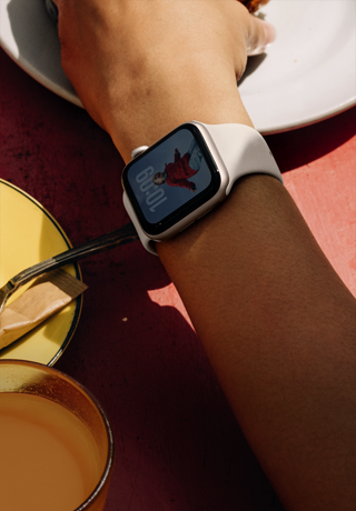 Bileğinde Yıldız Işığı renkte alüminyum kasaya sahip Apple Watch SE 3 takılı bir kişi kahvaltılıklara uzanıyor, hep açık ekran, kadranda bir kişinin fotoğrafı, yıldız ışığı renkte Spor Kordon