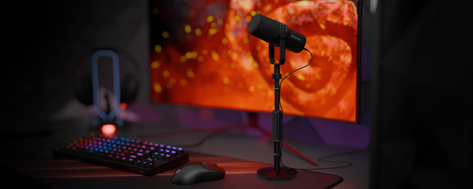 Microphone on a stand with a colorful keyboard, mouse, and a large monitor in the background